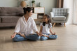 © fizkes - Indian woman laughing seated cross-legged on floor doing meditation practice with cute little daughter at modern cozy home. Loving parent teach child yoga, instill good habits for healthy lifestyle