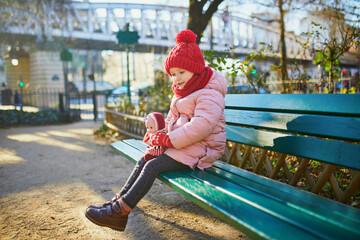 Wall Mural - Happy preschooler girl sitting on the bench on a street of Paris, France