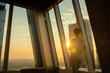 © zyabich - Back view of woman silhouette looking at cityscape through window of skyscraper. Summer time, sunset, warm illumination, lens flare. Success, opportunity, sightseeing, discover and future concept
