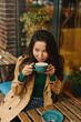 © olga pink - Portrait of young Asian woman drinking coffee witn apple pie in cafe on terrace of cafe. Outdoors. Cozy autumn season
