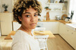 African american female blogger recording stories with her daily routing, posing at kitchen with window against dining table, going to cook and share process with her target audience in social media