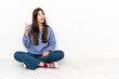 © luismolinero - Young woman sitting on the floor thinking an idea pointing the finger up
