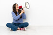 © luismolinero - Young woman sitting on the floor shouting through a megaphone