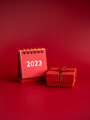 Wall Mural - Happy new year 2023 vertical backgrounds. 2023 numbers year on small red desk calendar cover and small present gift box isolated on red background, vertical style, minimalist.