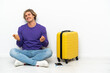 © luismolinero - Young blonde man with suitcase sitting on the floor making money gesture