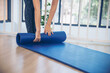 Home workout woman close up hands rolling foam yoga gym mat. Woman hands rolled up yoga mat on gym floor in yoga fitness training room. Woman barefoot home workout sportive healthy lifestyle concept