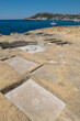 Chequerboard of rock-cut saltpans on the shoreline in Malta, Gozo on a nice summer day with boats anchored in the background.