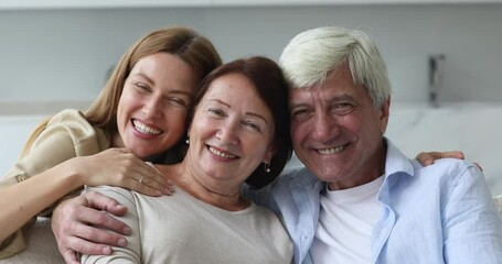 Wall Mural - Young woman her old pretty mom and hoary dad laughing, hugging, posing look at camera seated on sofa in living room, close up. Priceless time together with older parents, happy family portrait concept