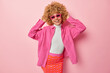 © wayhome.studio  - Indoor shot of cute curly haired woman wears sunglasses shirt and skirt keeps hands on head smiles gladfully feels happy to buy new clothes isolated over pink background. People and style concept