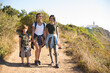 © KAMPUS - Portrait of smiling girls with preteen brother. Teen sisters walking with brother in countryside. Active family weekend concept