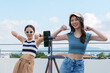 © Nattakorn - Young Asian woman with her friend tiktoker created her dancing video by smartphone camera together on rooftop outdoor at sunset. To share video to social media application