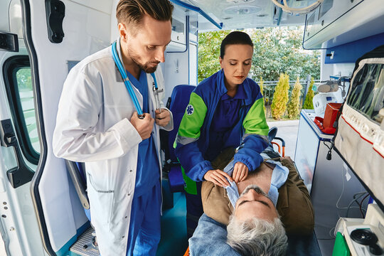 Paramedic in presence of doctor attaching ECG electrodes to male patient's chest to give him e electrocardiography examination inside ambulance. EMS