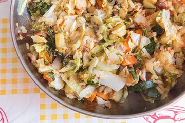 Wall Mural - Closeup of a silver bowl with colorful ingredients cooked in olive oil in a checkered background