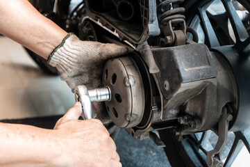 Mechanic using wrench and socket to Remove auto Transmission system or Rear Clutch Pulley of scooter Motorcycles,working in garage maintenance, repair motorcycle concept .selective focus