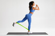 © nikolas_jkd - Fitness woman doing exercise for glutes with resistance band on gray background. Athletic girl working out.