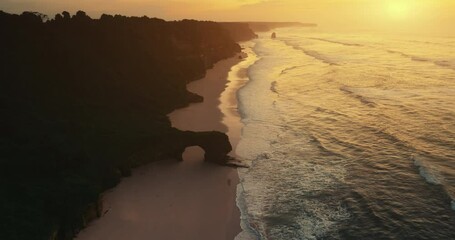 Wall Mural - Wavy sea rock wall giant hole aerial view. Orange sun set ocean waves wash sand beach top down drone shot. Cliff silhouette close up. Sandy coast soft evening sunlight. Tropical Hawaii vacation travel