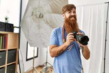 Wall Mural - Young redhead man photographer using professional camera at photograpy studio