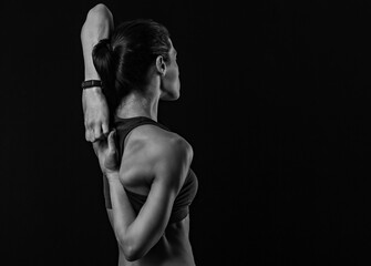 Wall Mural - Sporty healthy body woman with strong muscular shoulders and blades doing hands the lock exercise behind the back on black studio background with empty copy space.