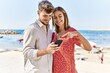 © Krakenimages.com - Young hispanic couple on vacation smiling happy using smartphone at the beach
