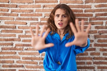 Sticker - Beautiful brunette woman standing over bricks wall doing stop gesture with hands palms, angry and frustration expression