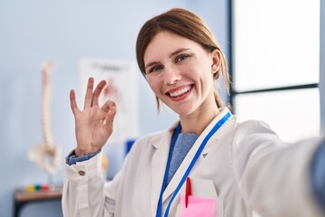 Sticker - Young physiotherapist woman working at pain recovery clinic doing ok sign with fingers, smiling friendly gesturing excellent symbol