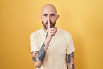 Poster - Hispanic man with tattoos standing over yellow background asking to be quiet with finger on lips. silence and secret concept.