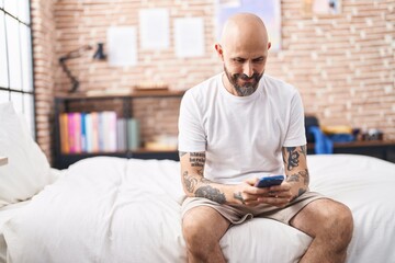 Sticker - Young bald man using smartphone sitting on bed at bedroom