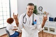 © Krakenimages.com - Middle age doctor man at the clinic with a patient shouting with crazy expression doing rock symbol with hands up. music star. heavy concept.