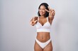 Hispanic woman wearing lingerie smiling with tongue out showing fingers of both hands doing victory sign. number two.