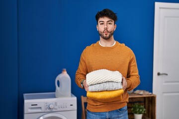 Sticker - Hispanic man with beard holding clean folded laundry making fish face with mouth and squinting eyes, crazy and comical.