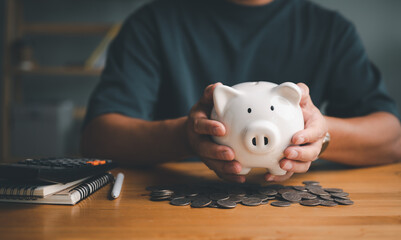 Man hand holding piggy bank on wood table, saving money wealth and financial concept, Business, finance, investment, Financial planning..