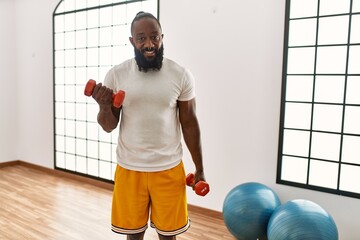 Wall Mural - Young african american man smiling confident training with dumbbells at sport center