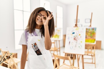 Poster - Young african american girl painting at art studio smiling happy doing ok sign with hand on eye looking through fingers