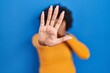 © Krakenimages.com - Black woman with curly hair standing over blue background covering eyes with hands and doing stop gesture with sad and fear expression. embarrassed and negative concept.