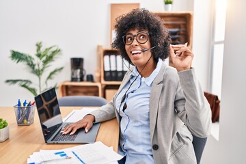 Sticker - Black woman with curly hair wearing call center agent headset at the office smiling amazed and surprised and pointing up with fingers and raised arms.