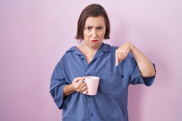 Sticker - Middle age hispanic woman drinking a cup coffee pointing down looking sad and upset, indicating direction with fingers, unhappy and depressed.