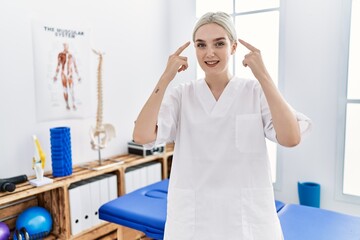 Sticker - Young caucasian woman working at pain recovery clinic smiling pointing to head with both hands finger, great idea or thought, good memory