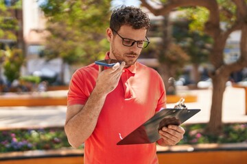 Poster - Young hispanic man talking on the smartphone reading document at park