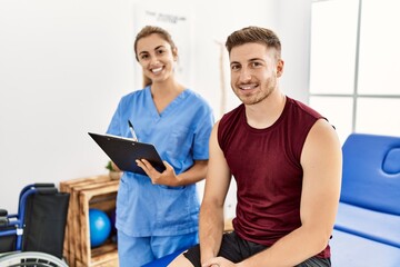 Wall Mural - Young hispanic physioterapist woman explain diagnosis to patient man at the clinic.