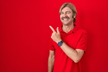 Sticker - Caucasian man with mustache standing over red background cheerful with a smile of face pointing with hand and finger up to the side with happy and natural expression on face