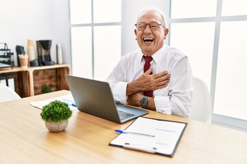 Canvas Print - Senior man working at the office using computer laptop smiling and laughing hard out loud because funny crazy joke with hands on body.