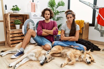 Wall Mural - Young hispanic couple doing laundry with dogs skeptic and nervous, disapproving expression on face with crossed arms. negative person.