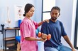 © Krakenimages.com - Man and woman wearing physiotherapist uniform having rehab session using dumbbell at physiotherpy clinic