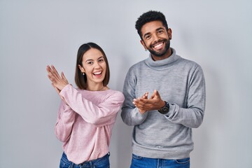 Canvas Print - Young hispanic couple standing together clapping and applauding happy and joyful, smiling proud hands together