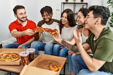 Group of young friends smiling happy eating italian pizza sitting on the sofa at home.