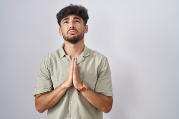 Wall Mural - Arab man with beard standing over white background begging and praying with hands together with hope expression on face very emotional and worried. begging.