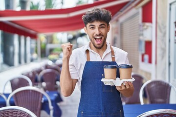 Sticker - Arab man with beard wearing waiter apron at restaurant terrace screaming proud, celebrating victory and success very excited with raised arms