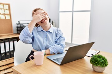 Wall Mural - Young redhead woman working at the office using computer laptop smiling and laughing with hand on face covering eyes for surprise. blind concept.