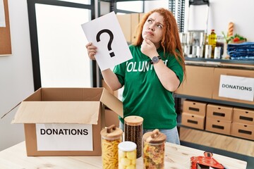 Canvas Print - Young redhead woman wearing volunteer t shirt holding question mark serious face thinking about question with hand on chin, thoughtful about confusing idea