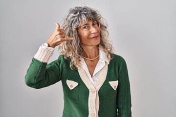 Wall Mural - Middle age woman standing over white background smiling doing phone gesture with hand and fingers like talking on the telephone. communicating concepts.